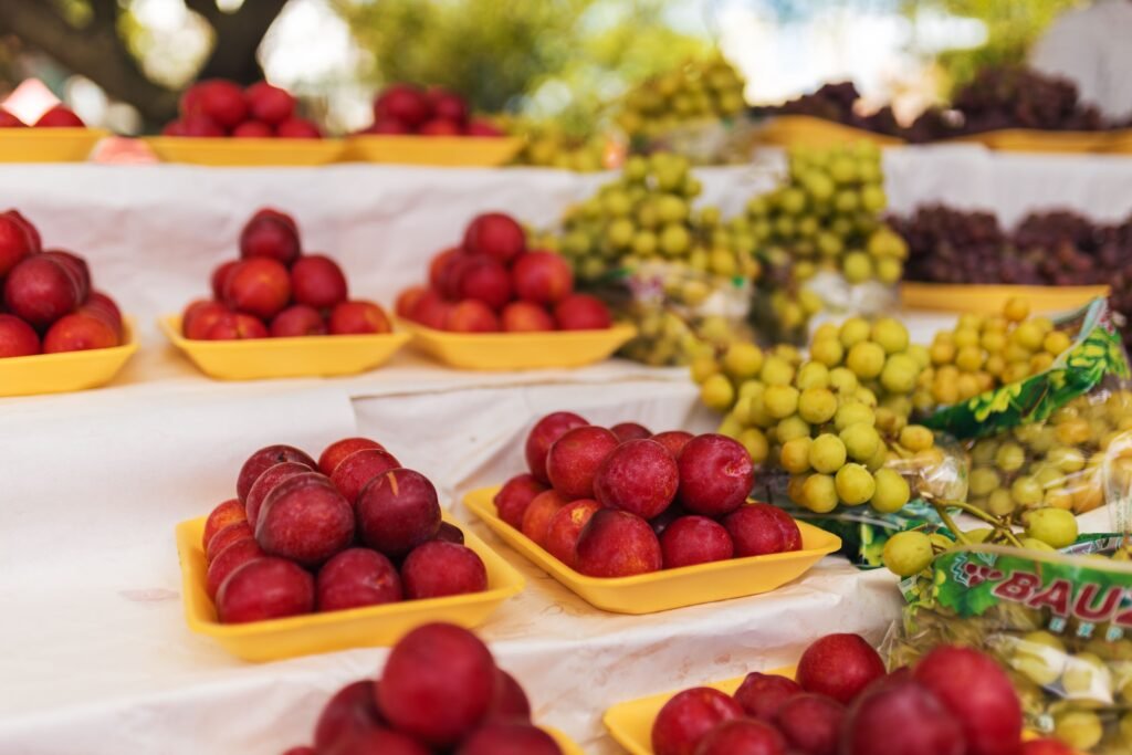 Vibrant display of fresh plums and grapes at an outdoor market with yellow trays.