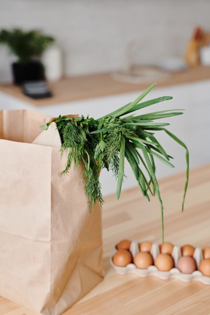 Organic groceries with brown eggs, leafy greens, and paper bag on kitchen counter.